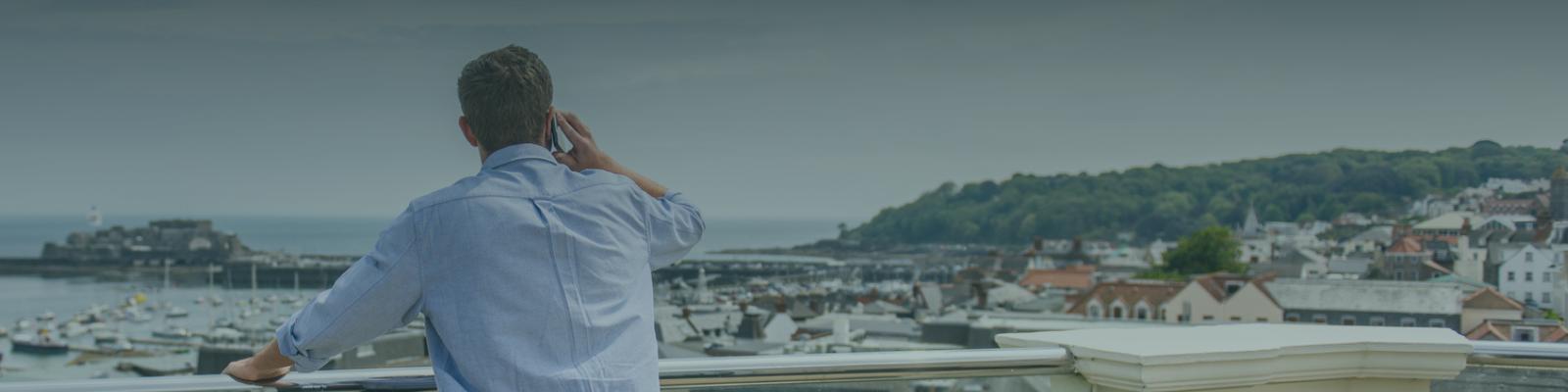 a man stood on a balcony on the phone overlooking St Peter Port